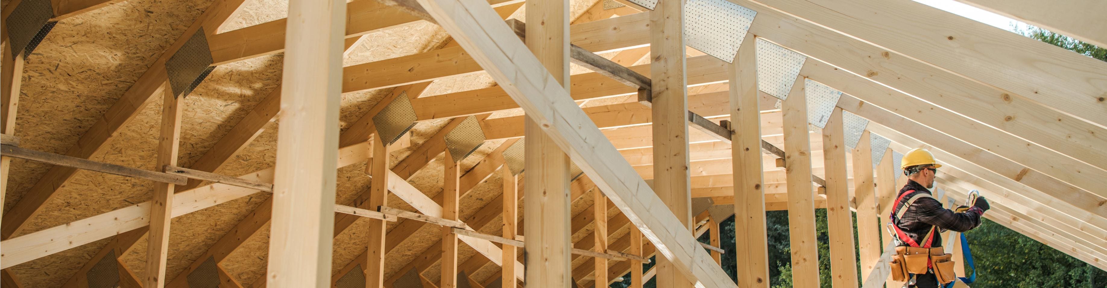 Construction worker in a yellow hard hat and safety harness installing wooden roof trusses