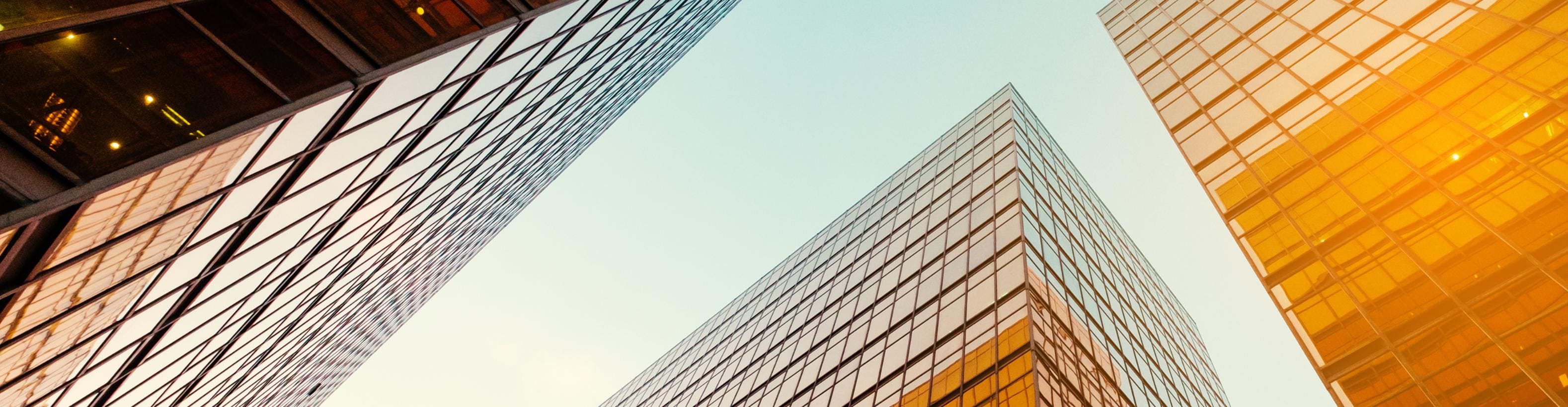 Low-angle view of modern glass skyscrapers reflecting golden sunlight against a clear blue sky