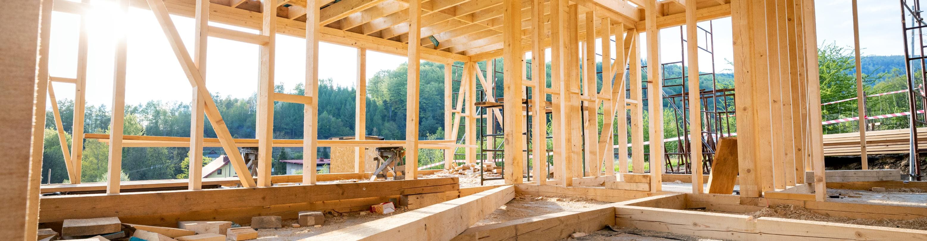 Interior wooden stud framing of a house under construction with forested hills visible through open walls