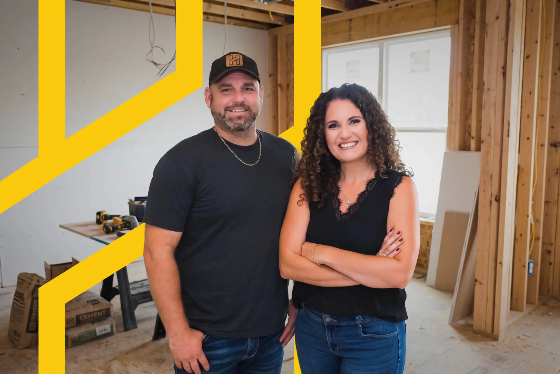 Jason and Liz Holley smiling inside a home under construction with exposed wood framing