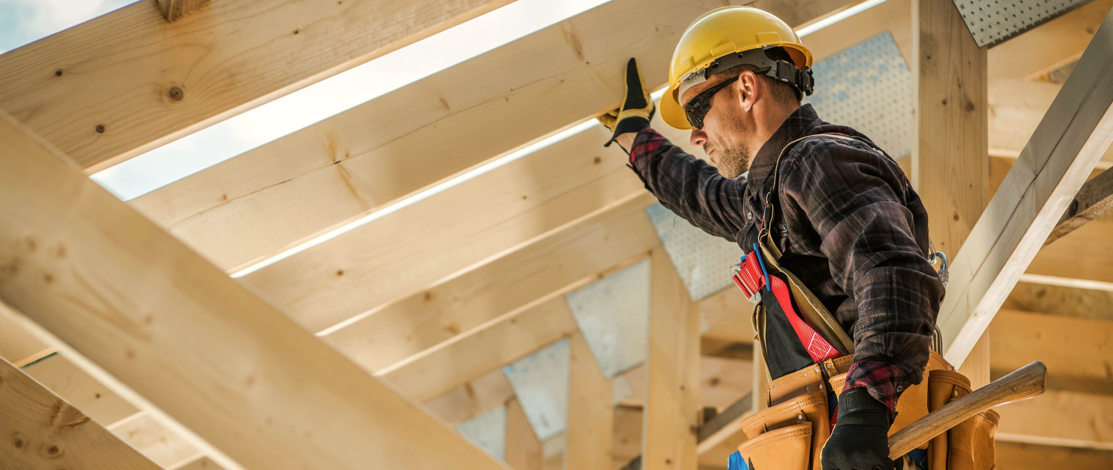 Construction worker in a yellow hard hat installing wooden roof framing