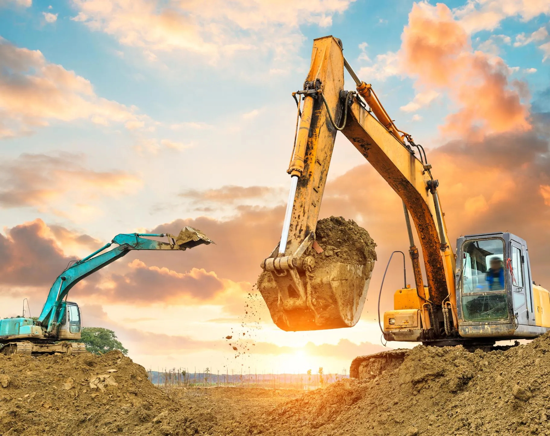 Yellow excavator lifting a bucket of earth at sunset next to a second excavator
