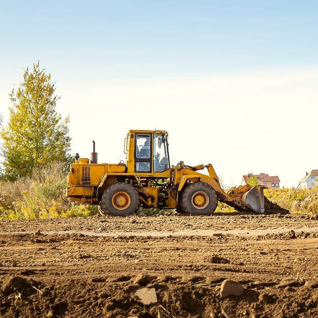 Yellow front-end loader parked on a dirt construction site under a clear sky