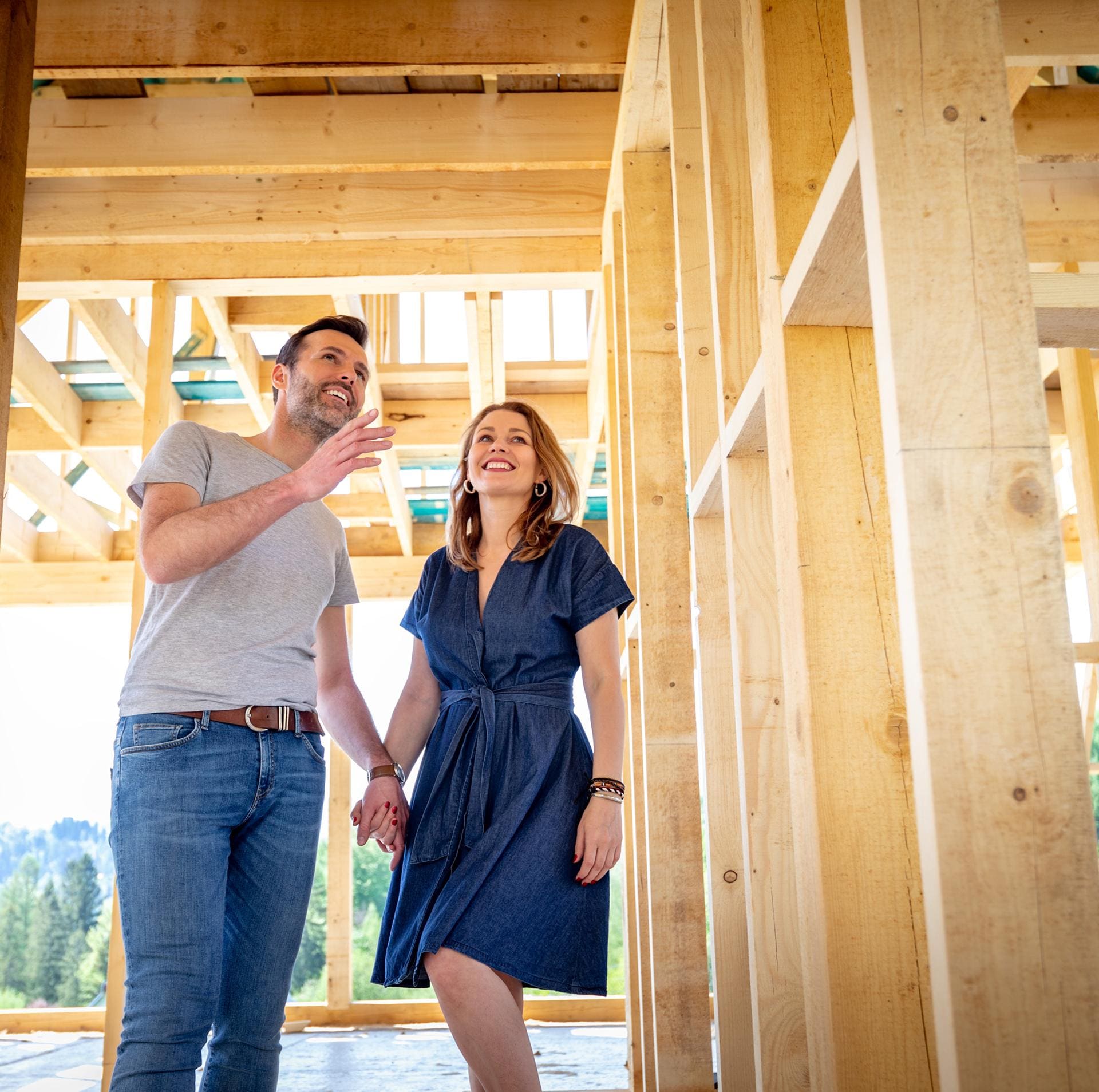 Smiling couple holding hands inside the wooden frame of a new home under construction