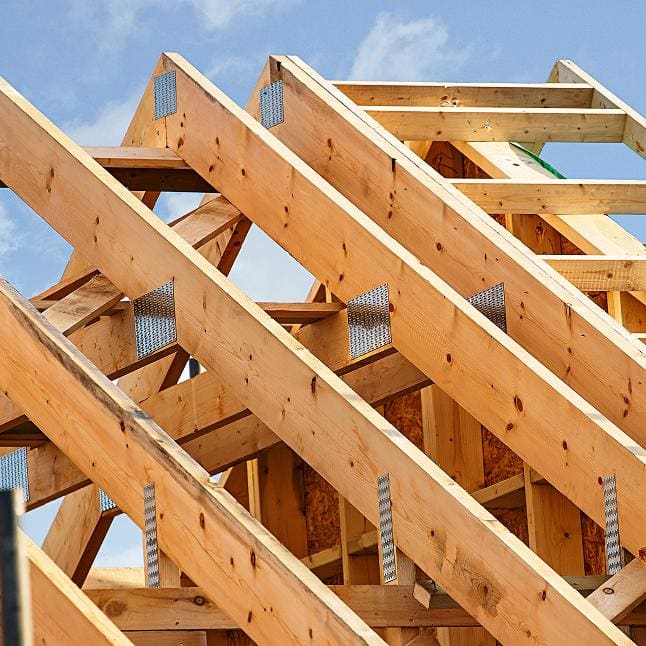 Close-up of wooden roof rafters joined with metal connector plates against a blue sky