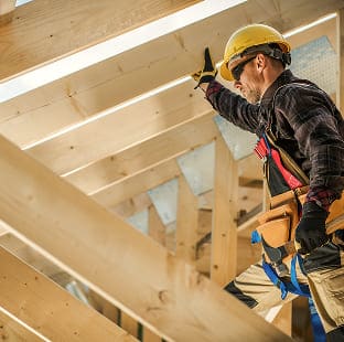 Construction worker in a yellow hard hat inspecting wooden roof rafters