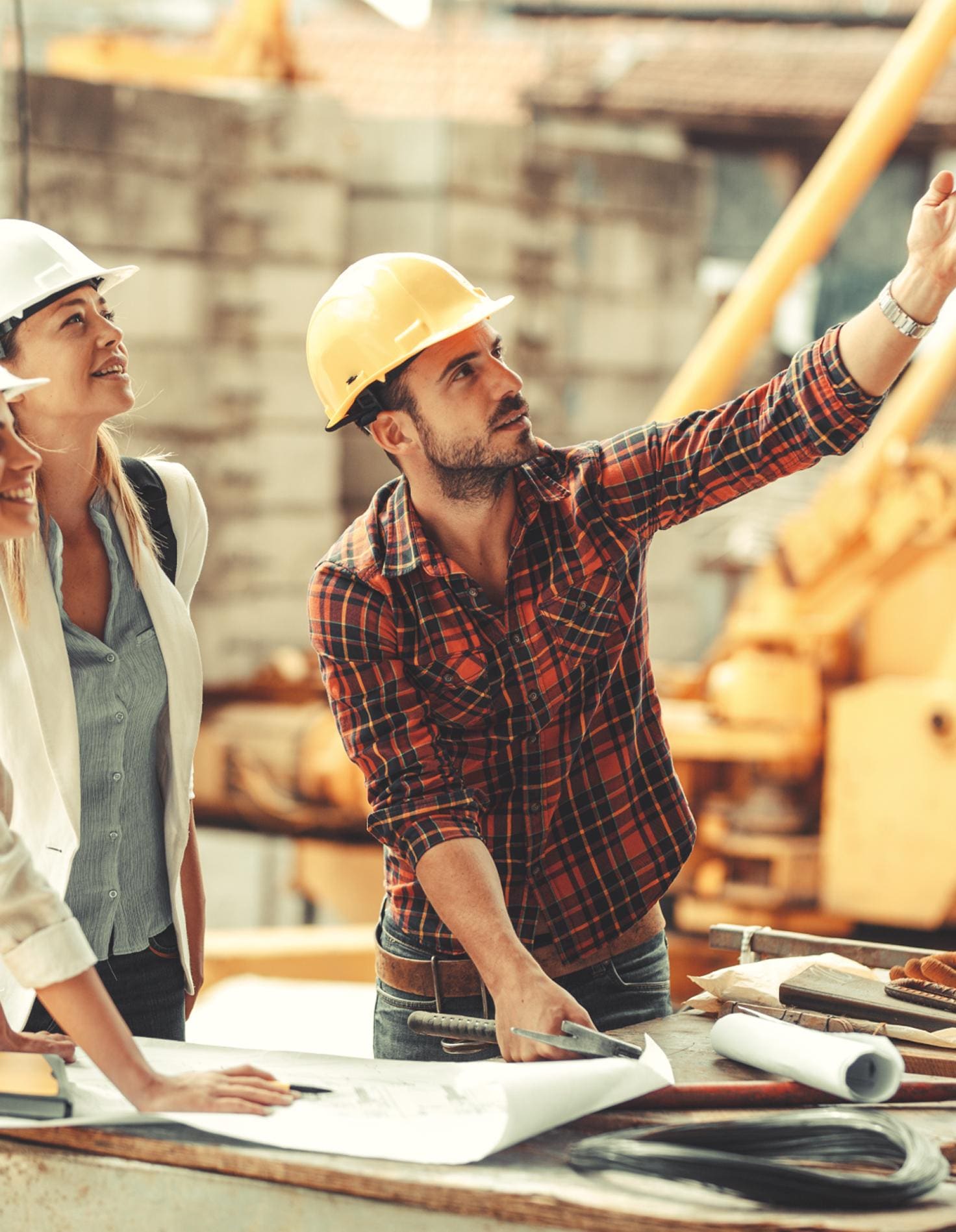 Construction team reviewing blueprints on a job-site workbench with a crane behind them